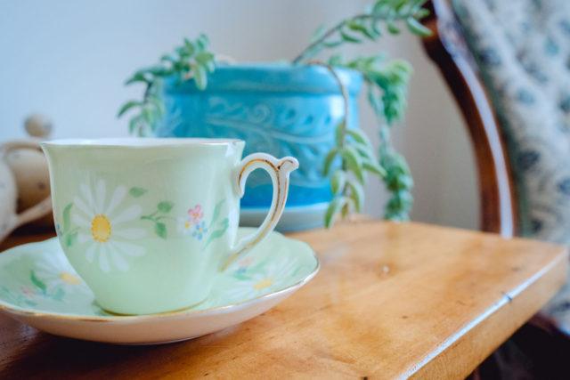 light green tea cup with a flowery design and a blue planter in the background