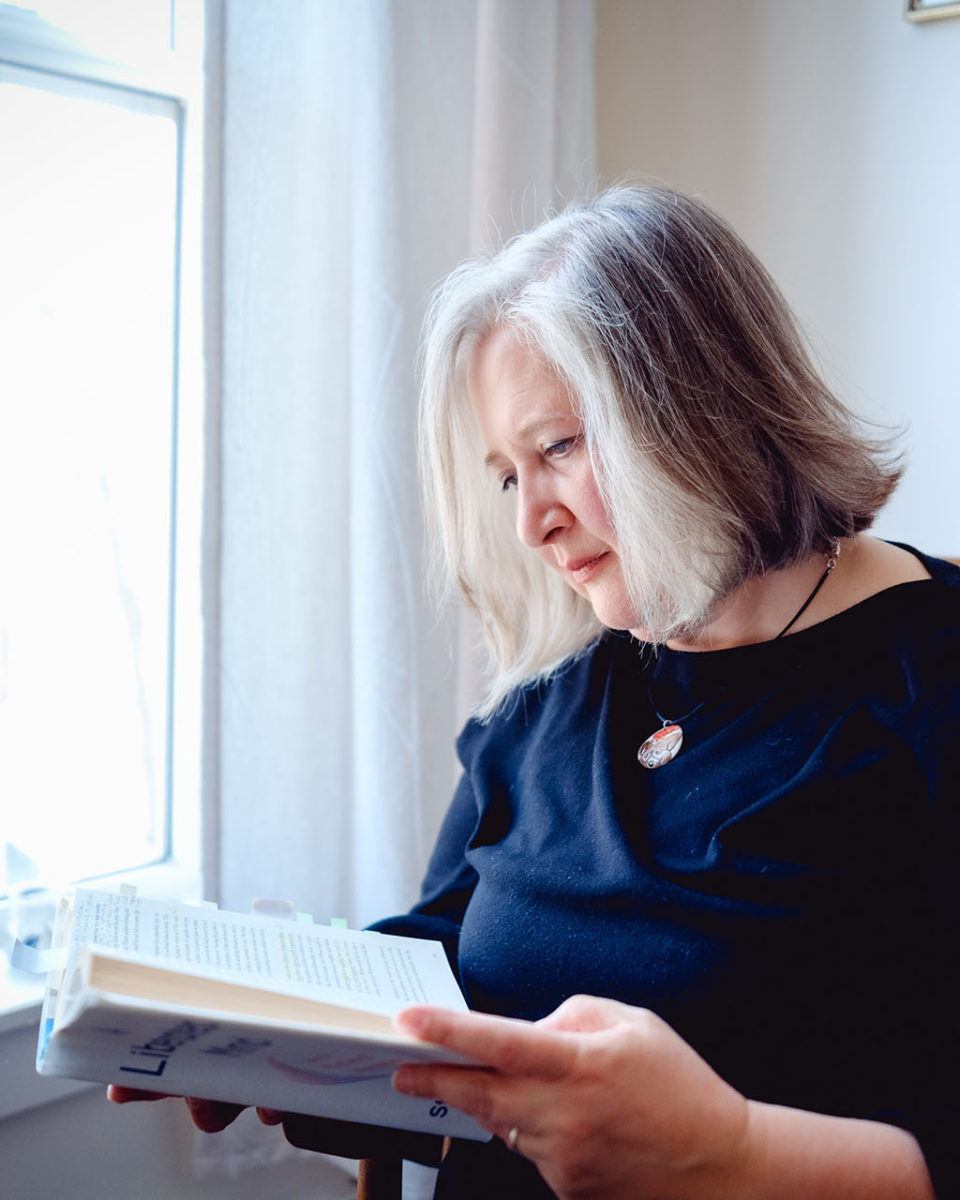 janet mcdonald reading a book beside a window